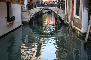 Fototapeta na wymiar Canals of Venice on a bright summer day. Typical canal of Venice, with the reflection of houses and the sky in the water, an old bridge with wrought iron railings.