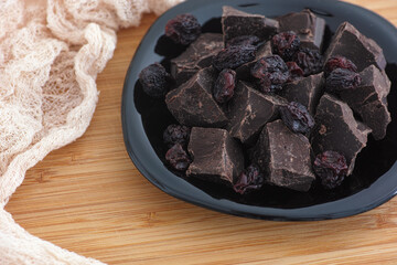 Pieces of homemade broken dark chocolate and raisins on a black plate
