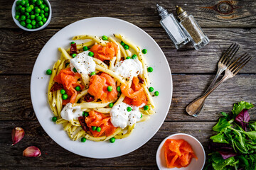 Maccheroni al ferretto with salmon nuggets, peas and sun-dried tomatoes on wooden table