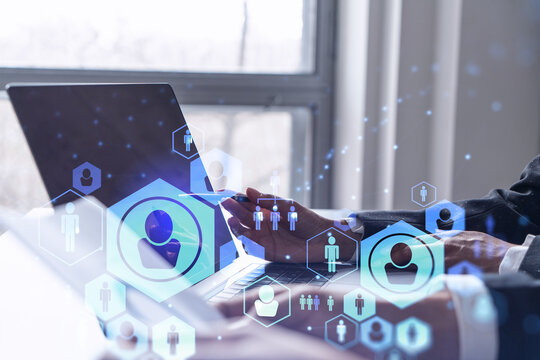 Two HR specialists analyzing the recruitment market using laptop to boost the intern program at international consulting company. Social networking hologram icons. - Powered by Adobe