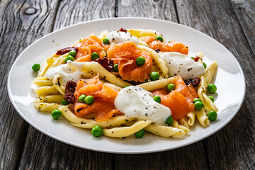 Maccheroni al ferretto with salmon nuggets, peas and sun-dried tomatoes on wooden table