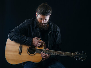 Obraz premium Bearded man sitting playing an acoustic guitar