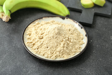 Plate with banana flour on dark background