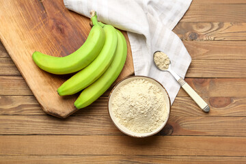 Bowl and spoon with banana flour on wooden background