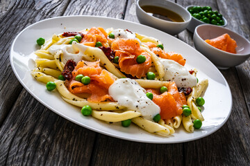 Maccheroni al ferretto with salmon nuggets, peas and sun-dried tomatoes on wooden table
