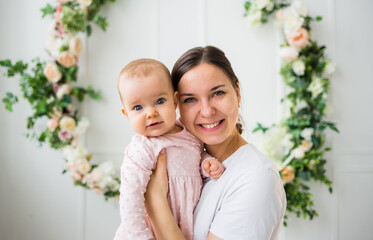 portrait of a beautiful brunette mom with a baby daughter in a pink dress on a white background with flowers