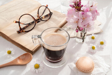 Black coffee in a cup next to a book with spring flowers on the table