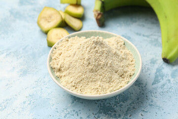 Bowl with banana flour on color background