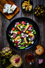 Fresh vegetable salad with feta cheese, artichokes, arugula, lettuce and cherry tomatoes on wooden table
