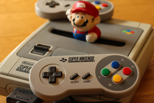 Closeup of a SNES (also know as Super NES) videogame consle, with its controller and a little Super Mario. The full name of the console is Super Nintendo Entertainment System