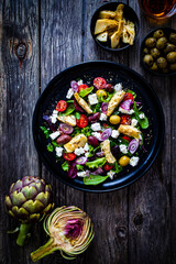 Fresh vegetable salad with feta cheese, artichokes, arugula, lettuce and cherry tomatoes on wooden table
