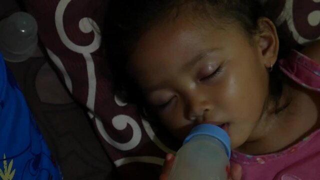 Portrait of little cute baby girl lies on bed sucks bottle of milk, drinks with big appetite. Baby food formula concept