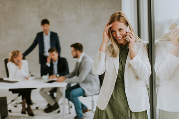 Young business woman standing in the office and using mobile phone in front of her team