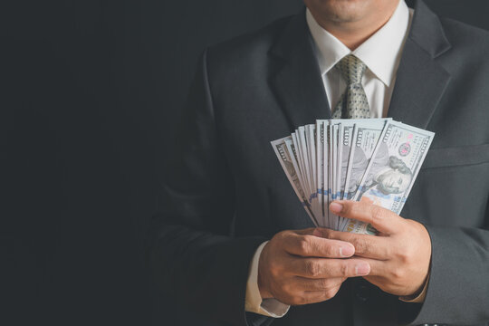 business man wearing suit and necktie holding money in hand on black background, US dollar (USD) bills