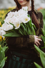Young woman gardener holds a bouquet of tulips grown in a greenhouse. Spring flowers and floriculture. Soft selective focus, defocus.