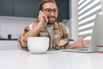 A cup of coffee is on the table against the background of a man talking on a mobile phone