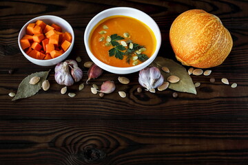 Vegetarian pumpkin cream soup in a white bowl decorated with seeds and herbs on a dark wooden table
