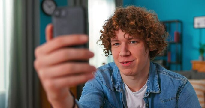 Portrait of happy 20s Caucasian man in casual clothing making facetime video calling with smartphone at home, smiling at people on phone screen. Using conferencing meeting online app, social
