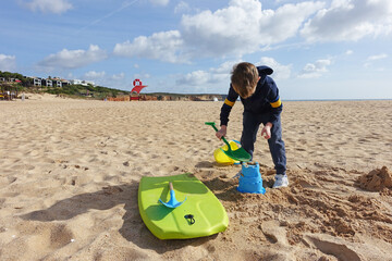 Little boy playing with a bucket and spade on the beach in winter