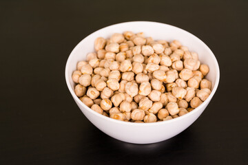 Pile of chickpeas in round white bowl on black table