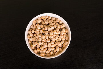 Pile of chickpeas in round white bowl on black table top view