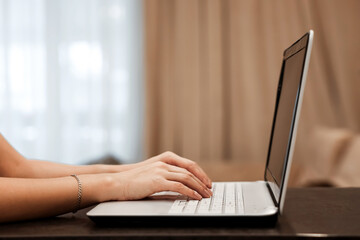 The hard hands of a businessman are typing on a laptop keyboard against the background of a blurred room. Concept for workplace, office, coworking, business, finance.