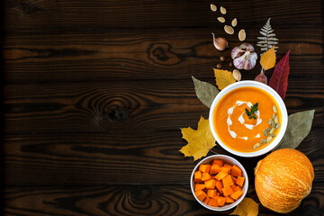 Vegetarian pumpkin cream soup in a white bowl decorated with seeds and herbs on a dark wooden table