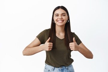 Cute smiling woman being supportive, showing thumbs up and looking happy, approve good choice, praise you, like or agree, standing over white background