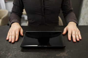 Male hands of a businessman next to a black tablet with a blank screen on the table, top view. Concept businessman, office, finance.