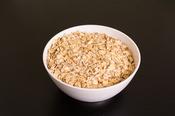 Pile of oats in round white bowl on black table top view