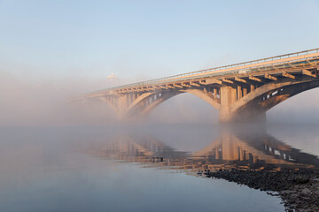 Naklejka premium A bridge over a large river.. Fog on the river in early spring
