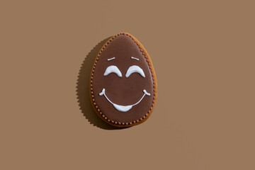 Festive bakery food. Cute gingerbread. Holiday gift. Theme party decor. Sweet egg figure cookie with chocolate icing white smiling face decoration isolated on beige copy space.