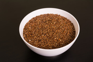 pile of Flax seeds in round white bowl on black table