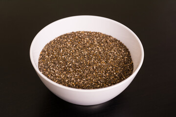 pile of chia seeds in round white bowl on black table top view