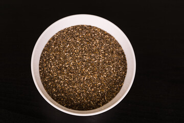 pile of Chia seeds in round white bowl on black table top view