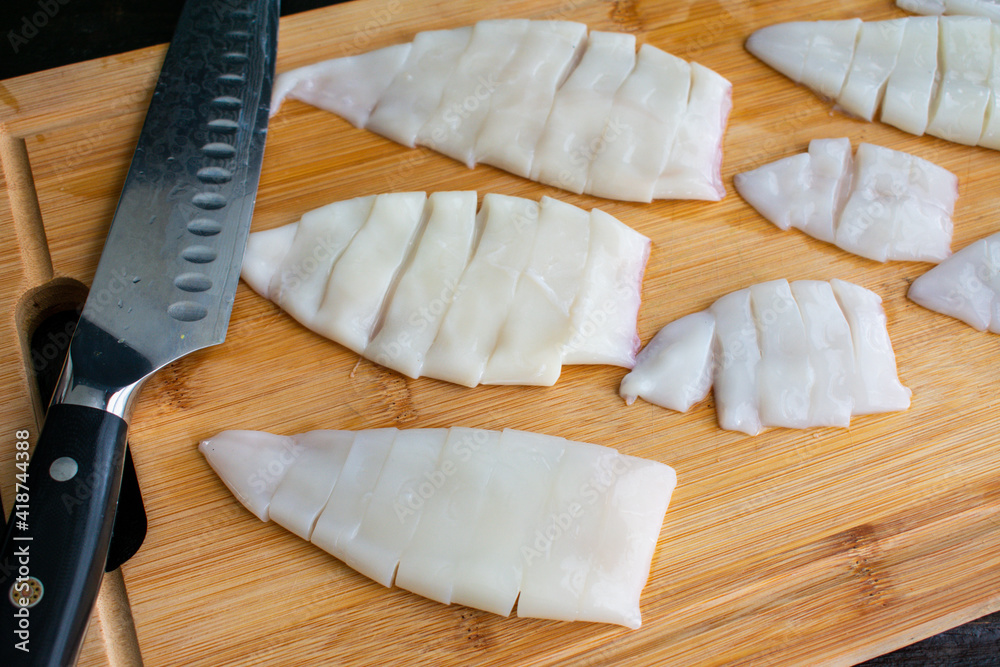 Wall mural sliced squid tubes on a bamboo cutting board: cleaned squid tubes being sliced into rings on a wood 