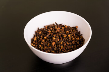 Pile of cloves in round white bowl on black table