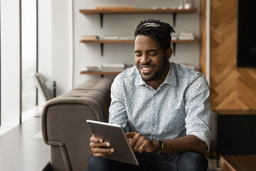 Close up smiling African American young man using tablet, browsing apps, chatting or shopping online, having fun with device, enjoying leisure time, playing game, reading news in social network