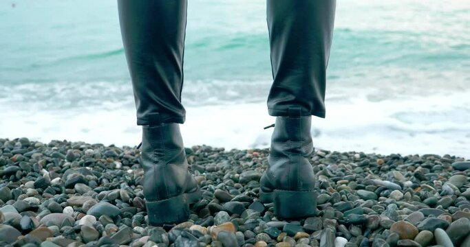 close-up of female feet in black boots on the pebble sea coast.