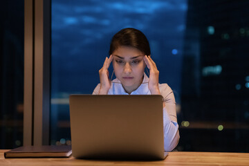 Close up stressed Indian businesswoman touching temples, working at night, using laptop, looking at screen, finishing project, preparing to deadline, overworked employee suffering from migraine