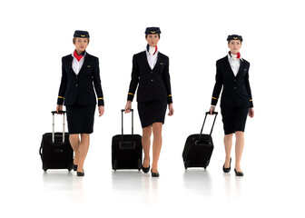 Three young and charming female flight attendants with trolley bags walking isolated on white background