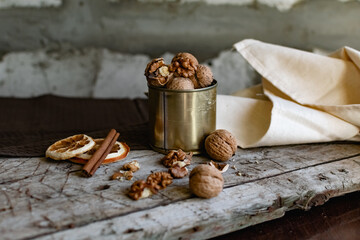 Walnuts in a tin of yellow metal next to the shell and the nuts on the inside. Decorated with dried oranges and a cinnamon stick. Composition of products and food on a wooden Board