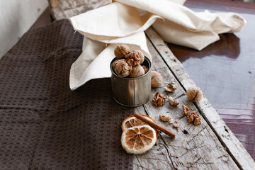 Walnuts in a tin of yellow metal next to the shell and the nuts on the inside. Decorated with dried oranges and a cinnamon stick. Composition of products and food on a wooden Board
