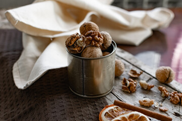 Walnuts in a tin of yellow metal next to the shell and the nuts on the inside. Decorated with dried oranges and a cinnamon stick. Composition of products and food on a wooden Board