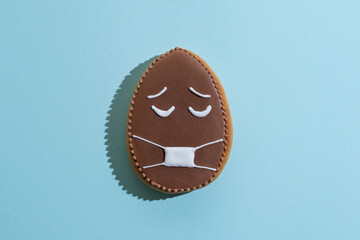 Pollution danger. Food decor. Bakery conceptual art. Sad egg gingerbread cookie with chocolate icing protective mask ornament isolated on blue textured.