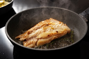 Cod fish fillet sautéed with thyme in a steaming frying pan on the black stove, copy space