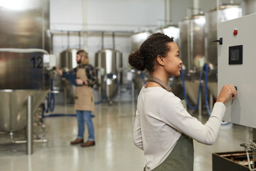 Side view portrait of young female worker operating machines in brewery workshop, copy space