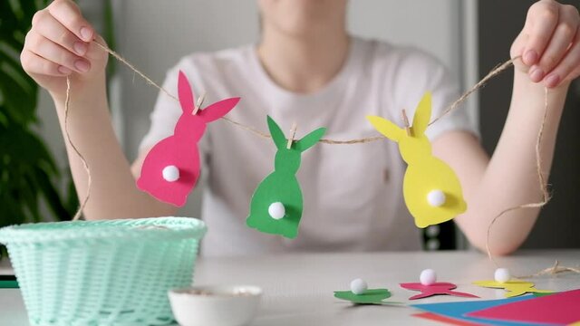 Boy made Easter paper garland. Multicolored Easter bunnies made of paper and pompons on string with clothespins