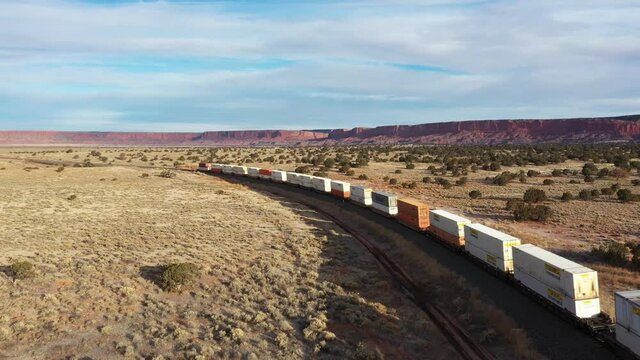 Train with containers double stacked on a wagon moving through the dessert on a partly cloudy day in the USA. Trucking shot