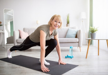 Positive athletic senior woman doing runner's lunge yoga pose on home workout, copy space